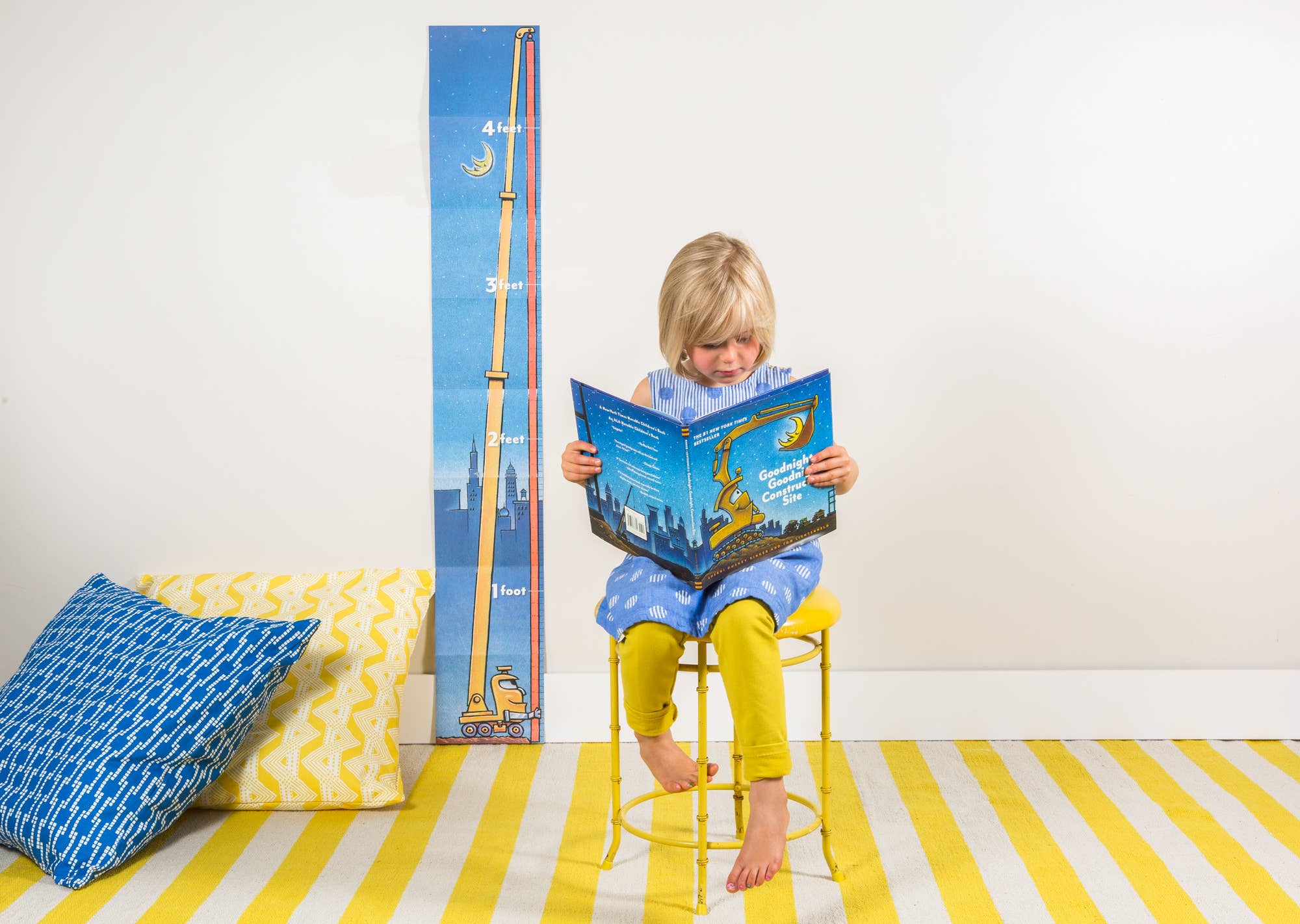 Child reading a book on a yellow stool with a growth chart in the background