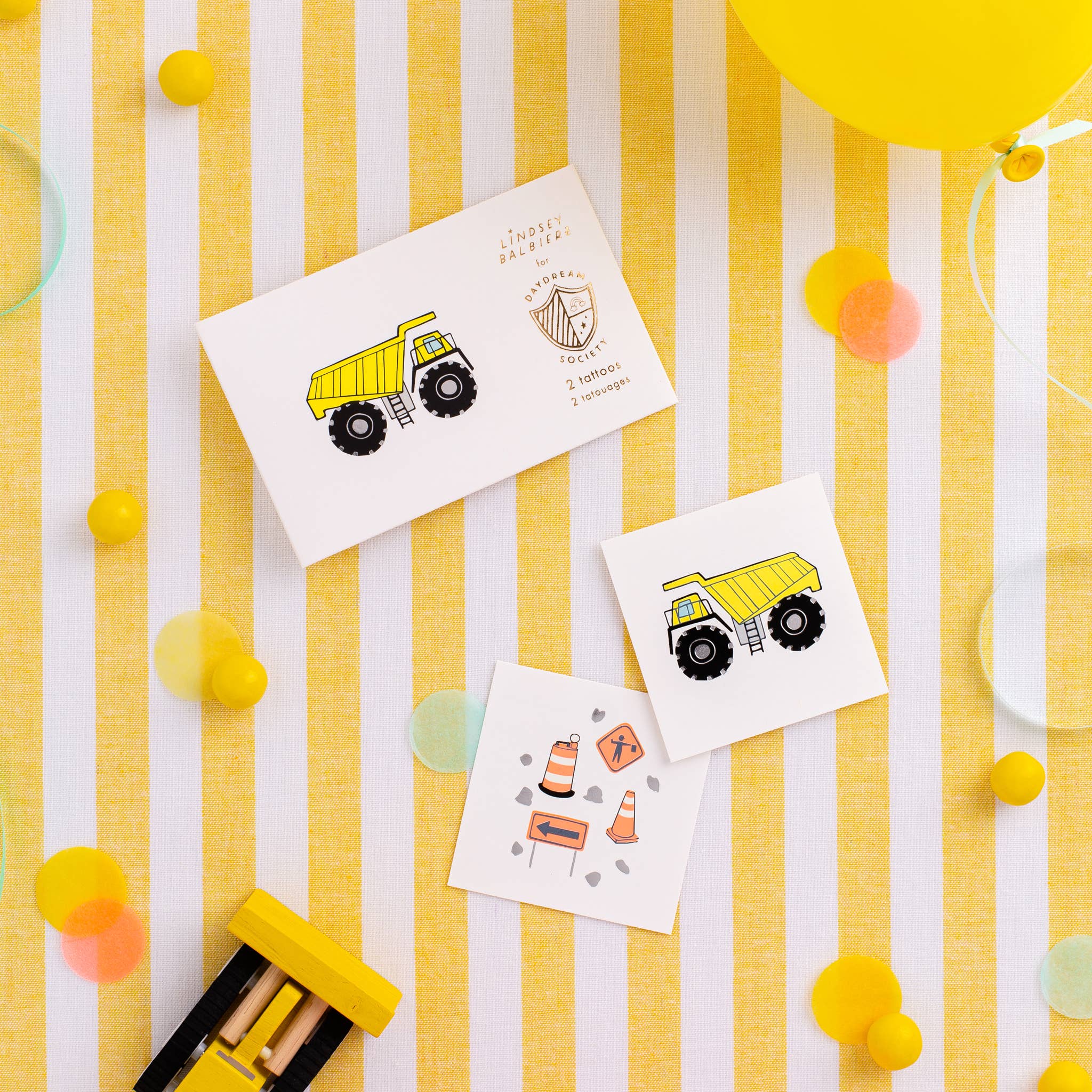 Children's temporary tattoos with construction vehicle designs on a yellow and white striped background.