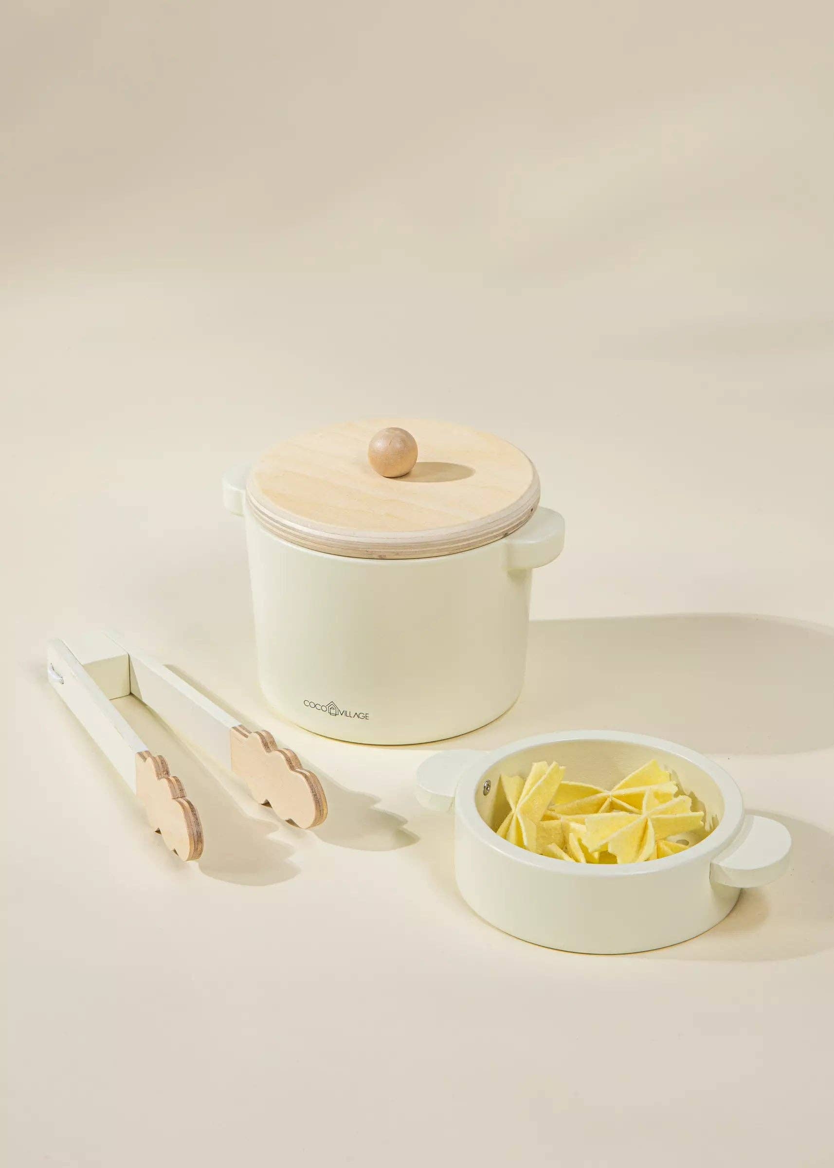 Small kitchen appliance with a lid, tongs, and a bowl of pasta on a light background