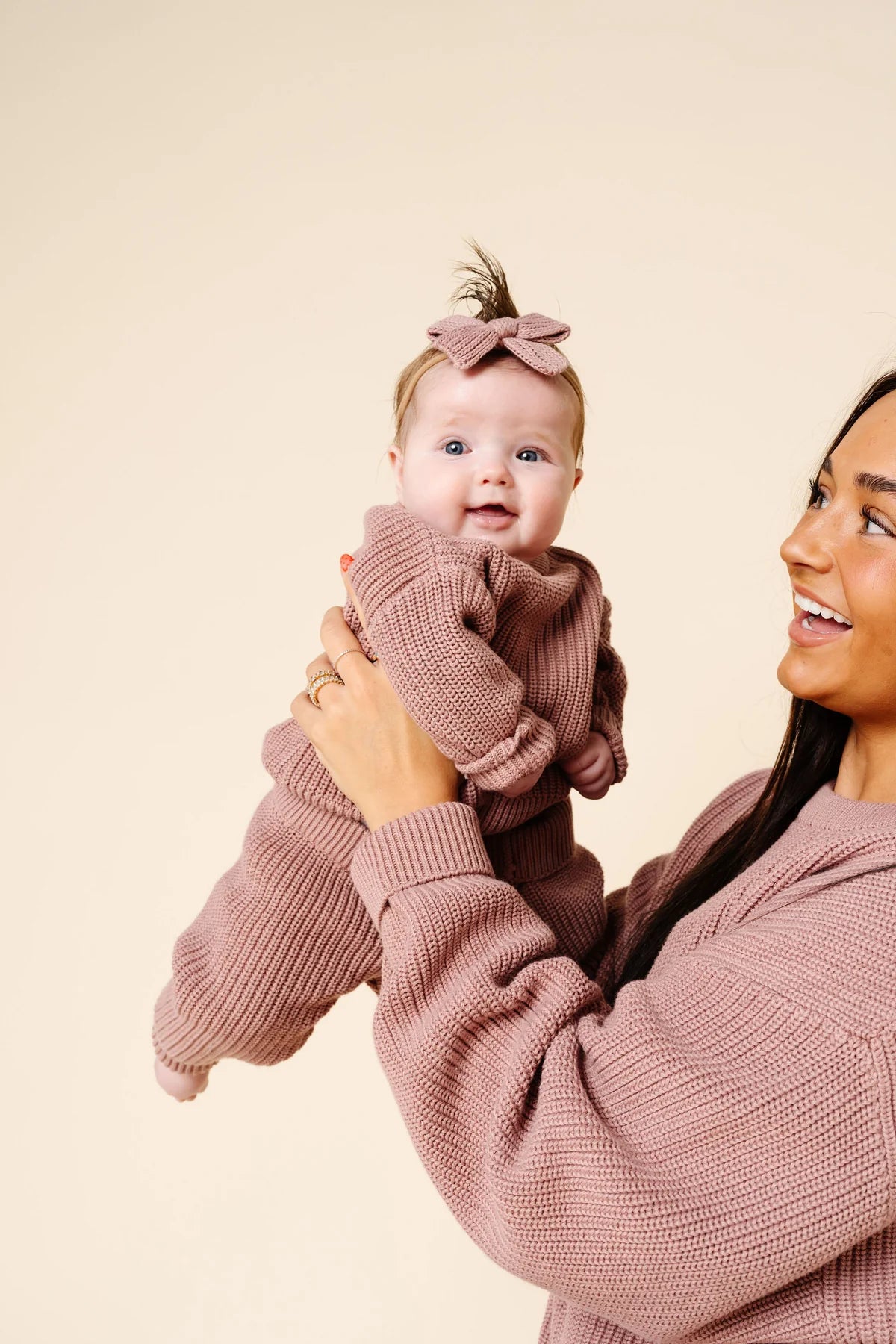 Woman holding a baby dressed in matching pink outfits against a beige background