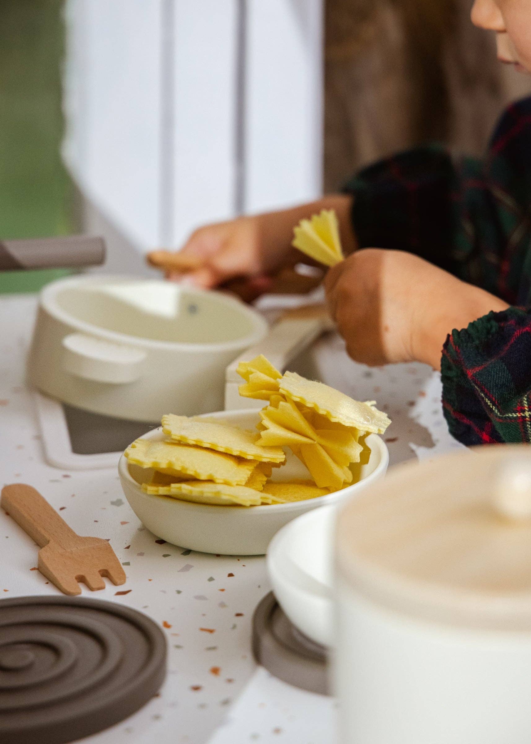 Children's play kitchen set with ceramic bowls and wooden utensils on a table.
