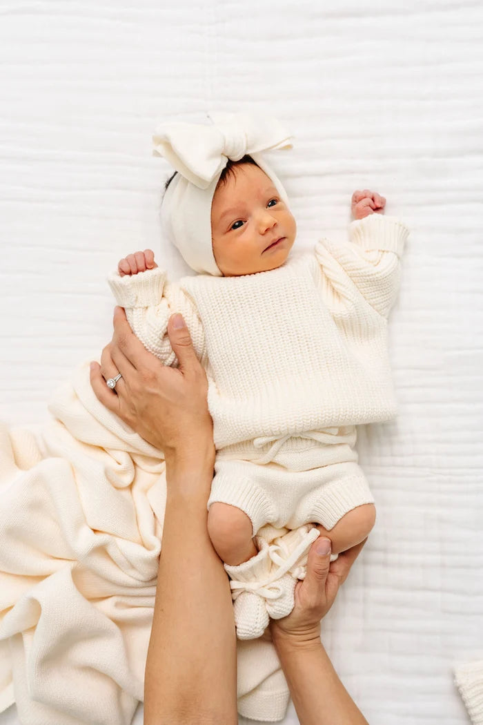 Newborn baby in a white outfit with a bow on a white blanket