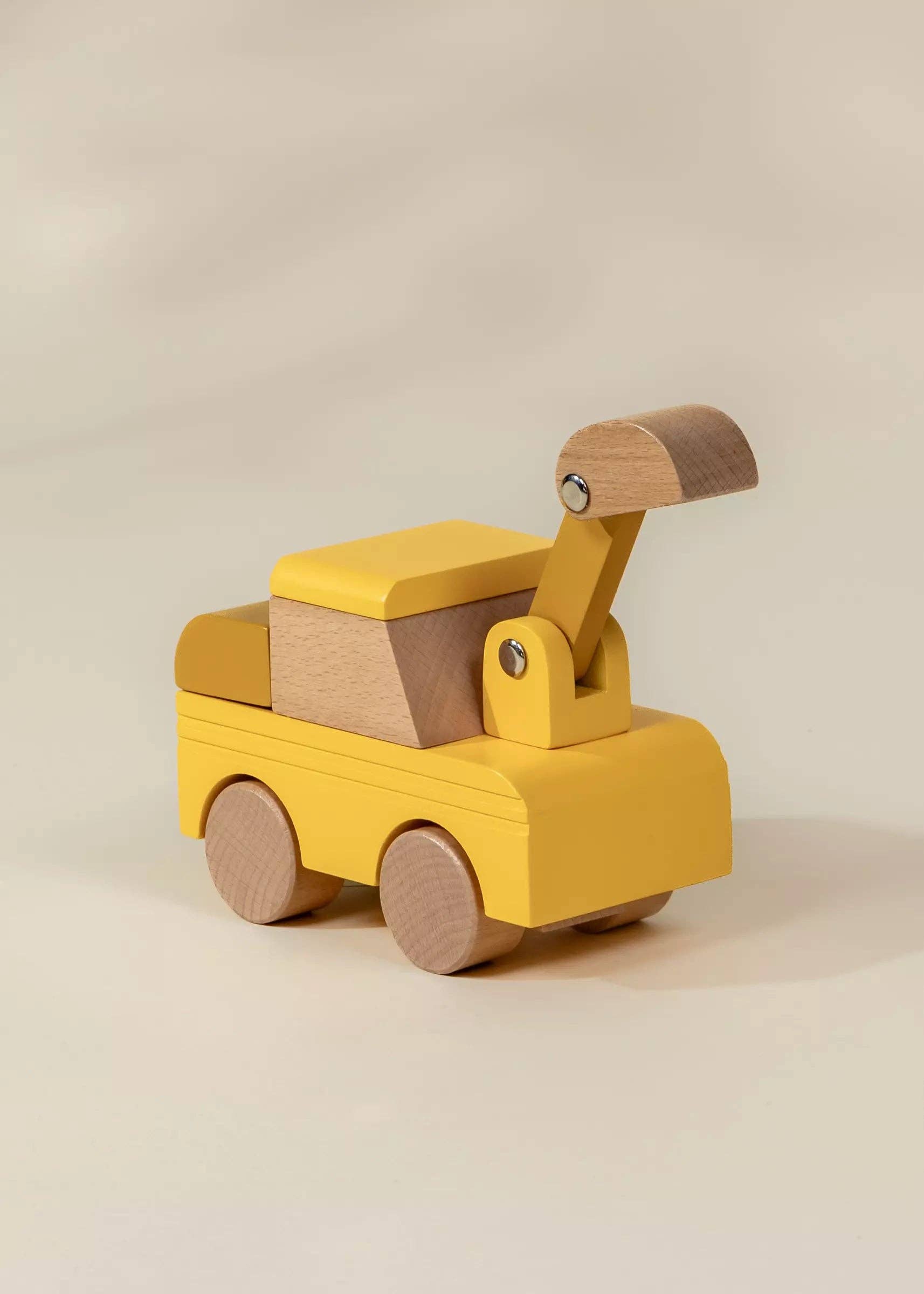 A wooden toy construction vehicle with a yellow painted body and natural wood accents, including the wheels and crane arm, photographed on a clean beige background.